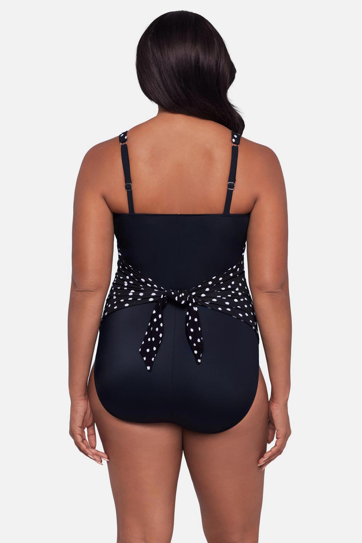 Woman turned away wearing a black and white polka dot one-piece swimsuit