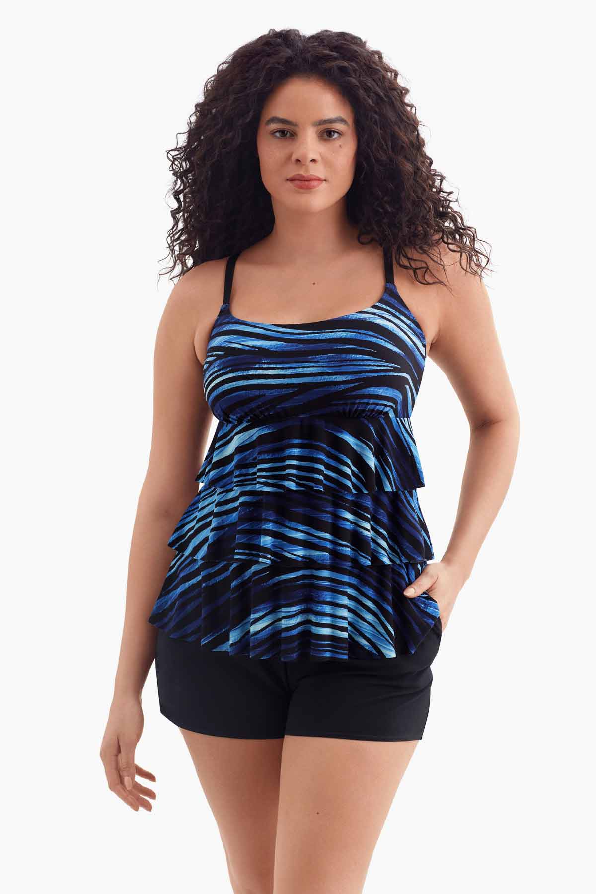 Woman wearing a one-piece tiered swimsuit with a black and blue print with her hand in pocket