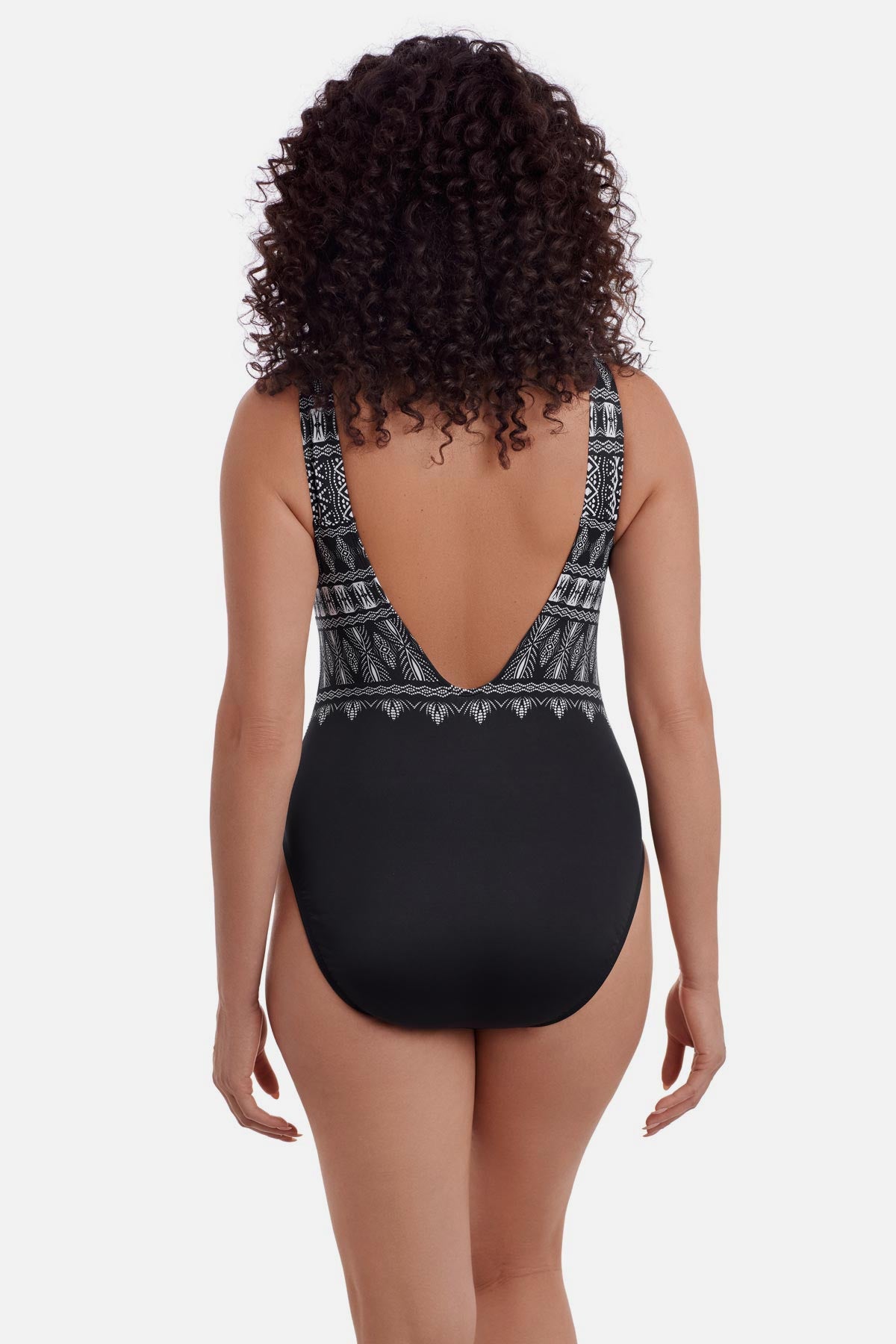 Woman turned away wearing a black and white tribal printed one-piece swimsuit with a deep scoop back