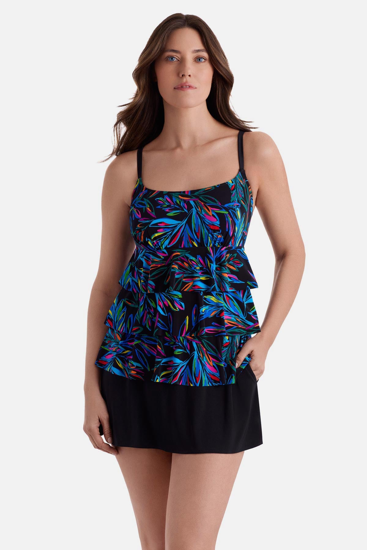 Woman wearing an abstract rainbow printed faux ruffle skirtini swimsuit with hand in pocket