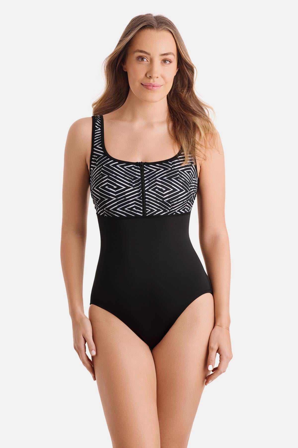 Woman wearing a black and white maze print one-piece swimsuit with a zipper down the front