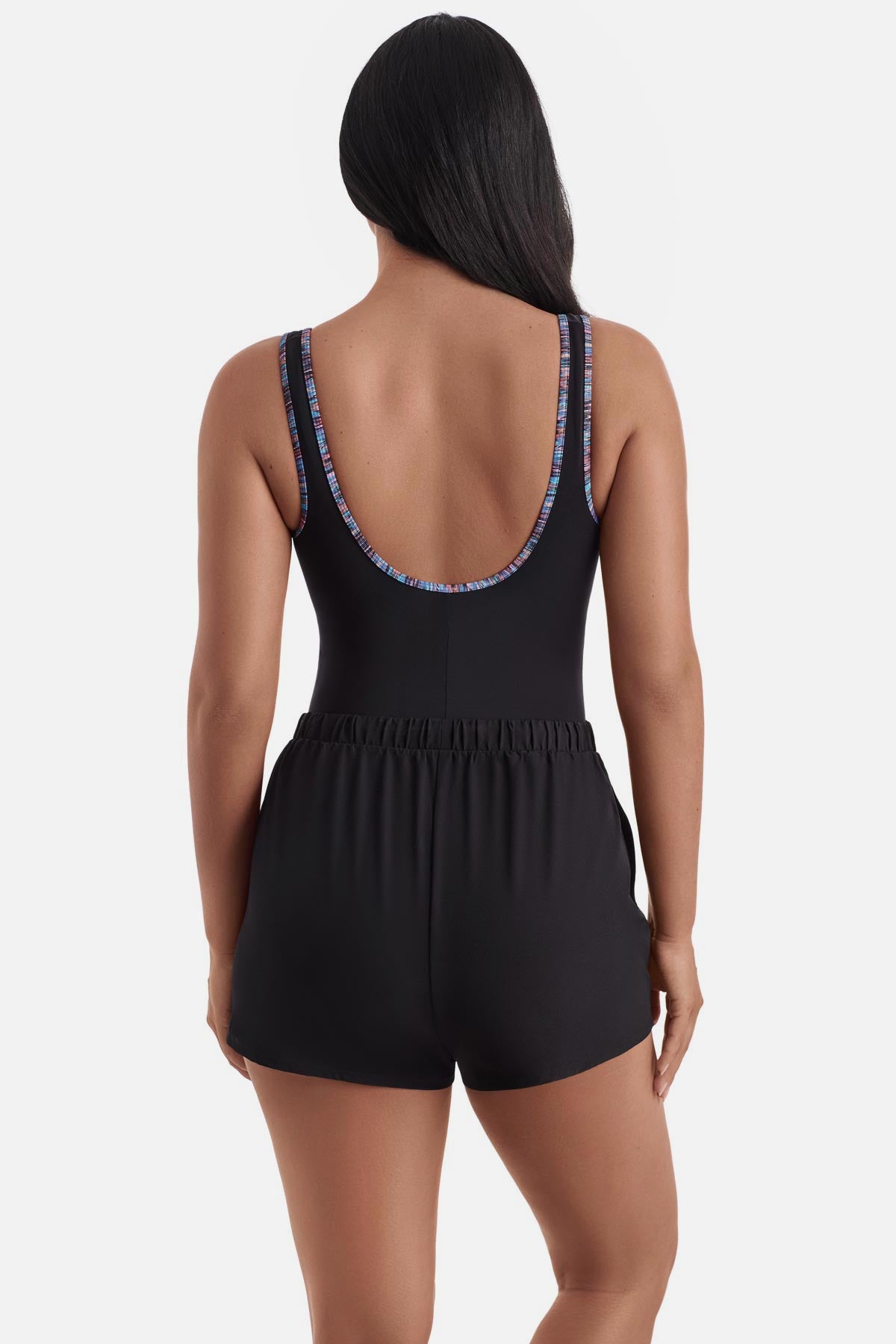 Woman turned away wearing a one-piece romper swimsuit with rainbow piping