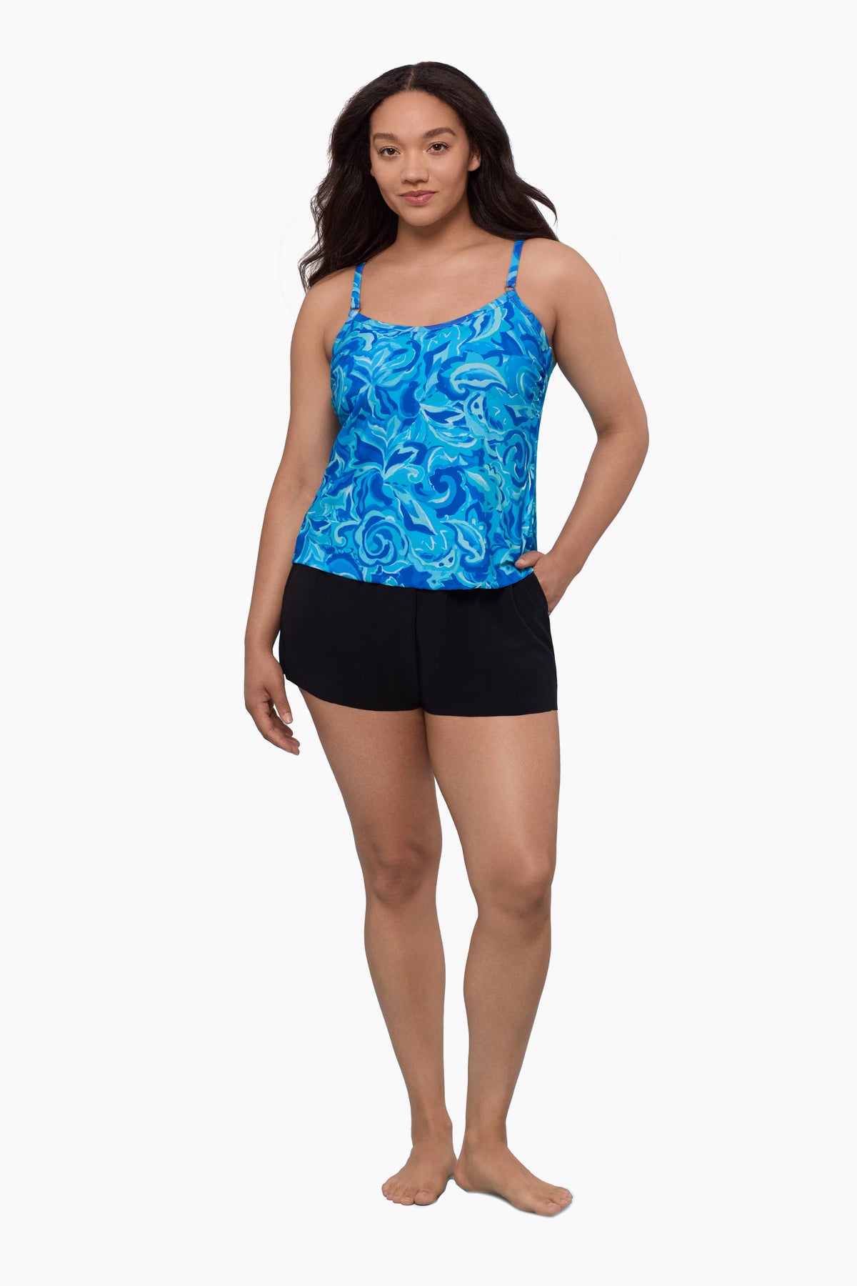Woman wearing a swim romper with an abstract blue print with hand in pocket 