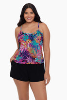 Woman wearing a swim romper with a neon palm leaf print and her hand in pocket