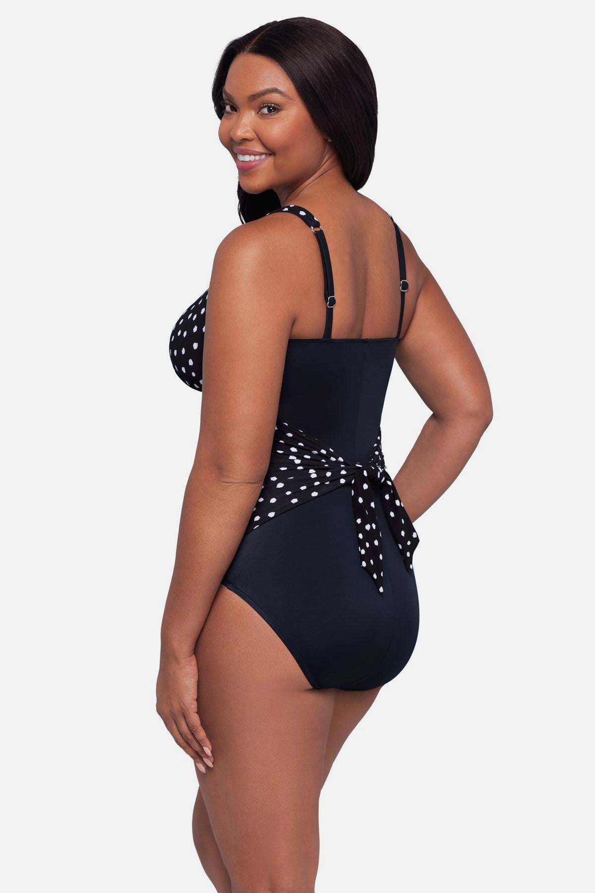 Woman turned left wearing a black and white polka dot one-piece swimsuit