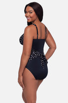 Woman turned left wearing a black and white polka dot one-piece swimsuit