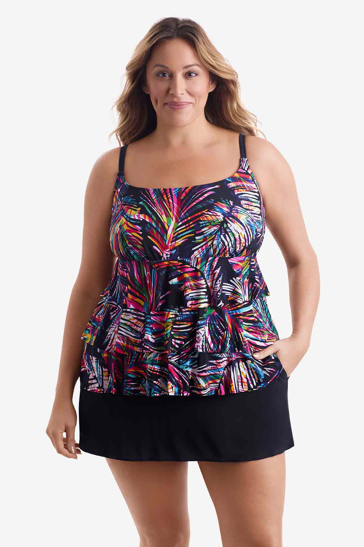 Woman wearing a tiered one-piece swimsuit with an abstract rainbow pattern with her hand in pocket