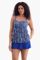 Woman wearing a tiered one-piece swimsuit with a blue and white pattern with her hand in pocket