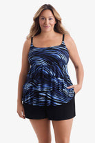 Woman wearing a tiered one-piece swimsuit with a black and blue pattern with hand in pocket