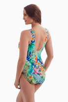 Woman turned to the side wearing a one-piece swimsuit with a multicolored palm leaf pattern