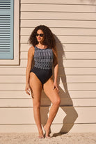 Woman leaned on wall wearing a black and white tribal printed one-piece swimsuit with a high neckline