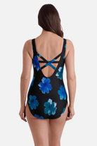 Woman turned awa wearing a one-piece swimsuit with large blue flowers and an X back