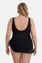 Woman faced away wearing a black one-piece swimsuit with a mesh sash around the waist