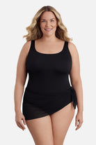 Woman wearing a black one-piece swimsuit with a mesh sash around the waist