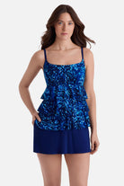 Woman wearing a blue abstract print ruffle skirtini swimsuit with hand in pocket