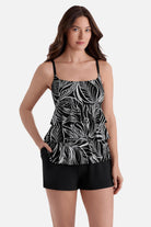 Woman wearing a black and white fern printed ruffle shortini swimsuit with hand in pocket