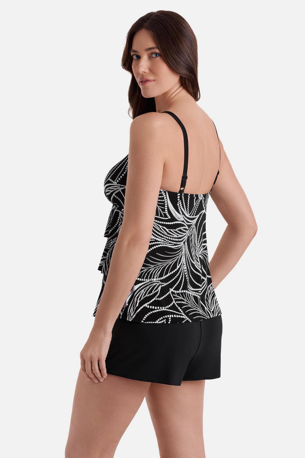 Woman turned left wearing a black and white fern printed ruffle shortini swimsuit