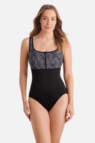 Woman wearing a black and white maze print one-piece swimsuit with a zipper down the front