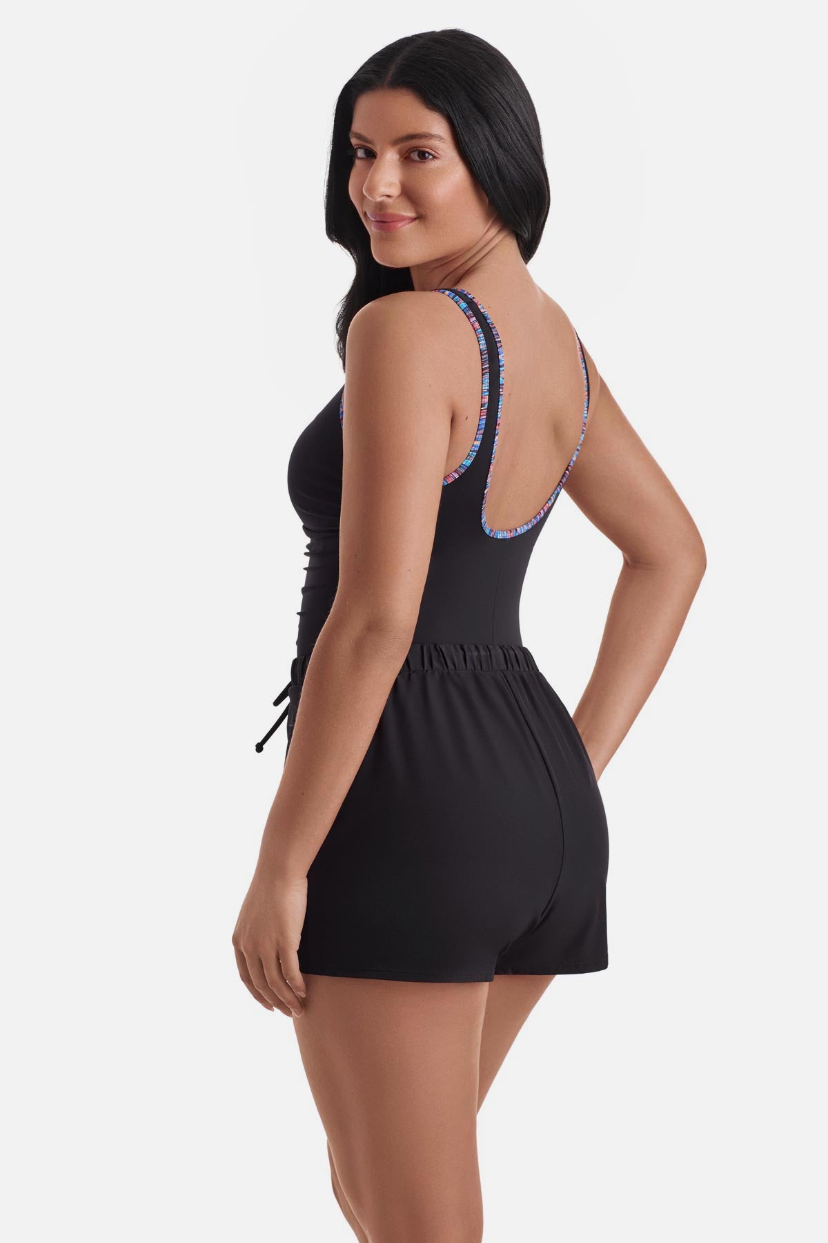 Woman turned left wearing a one-piece romper swimsuit with rainbow piping