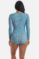 Woman turned away wearing a long sleeve one-piece swimsuit with a blue tile print