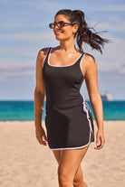 Woman on beach wearing a black swim dress with white piping/edges