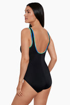 Woman turned left wearing a black one-piece swimsuit with blue and green piping on the straps