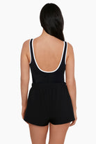 Woman faced away wearing a black swim romper with white piping on the edges